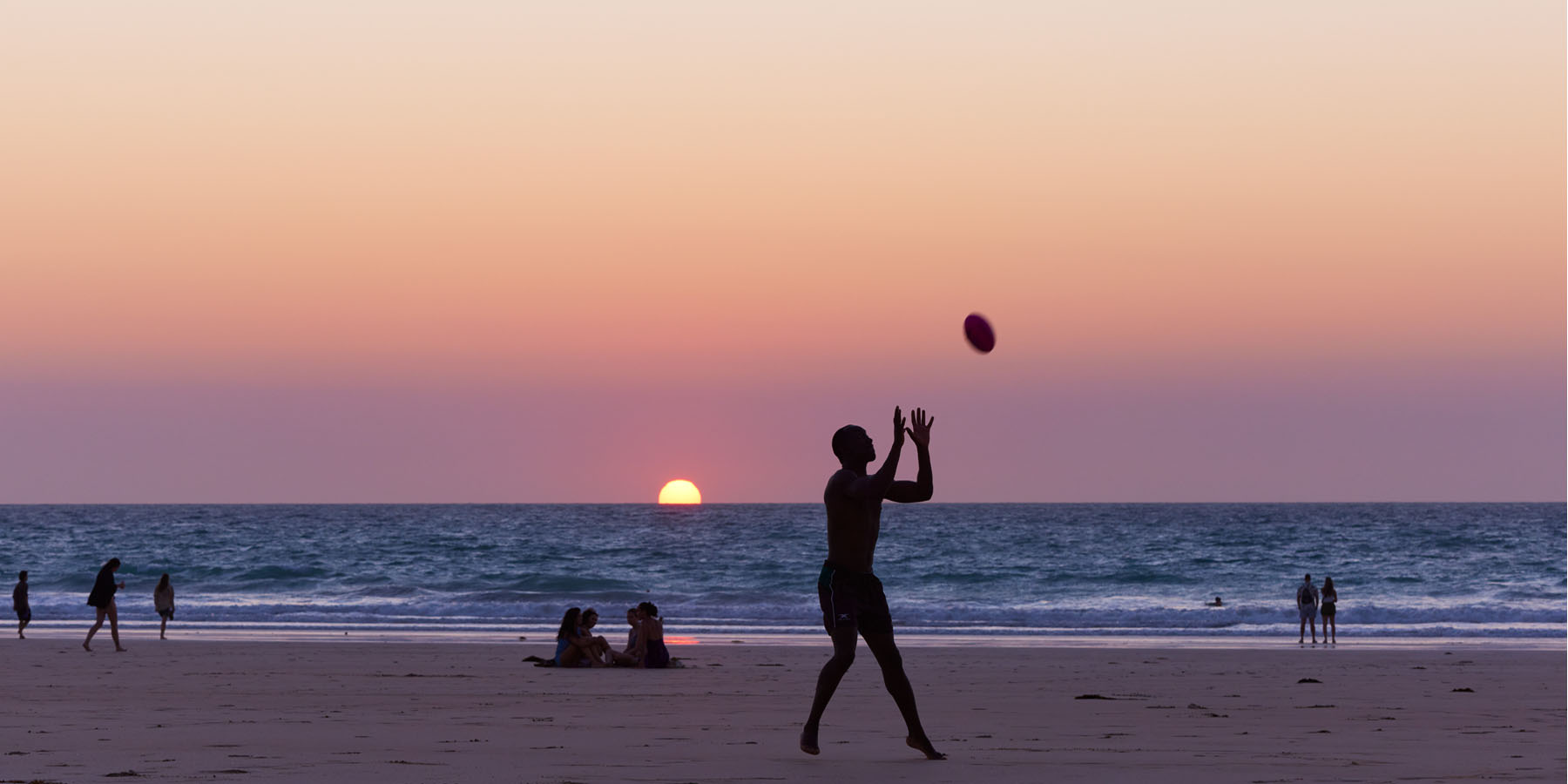 Image of man catching football as sun sets on Cable Beach